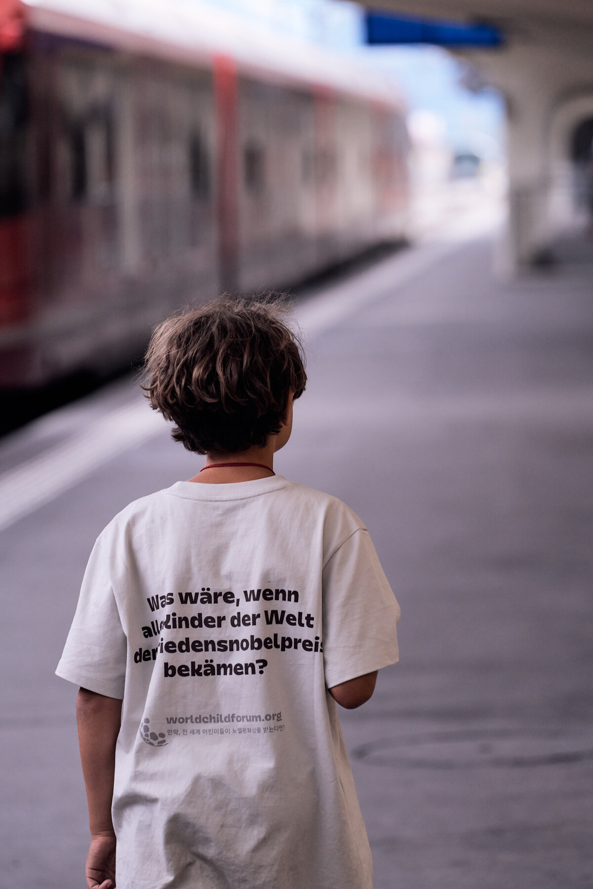 A boy on the Davos railway platform, his shirt asking what would happen if the children of the world received the Nobel Peace Prize