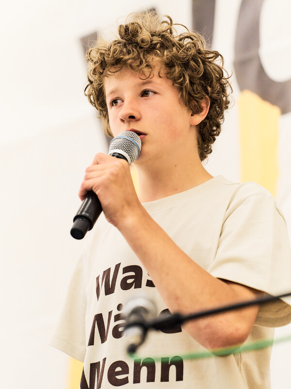 A boy with curly hair sings into a microphone